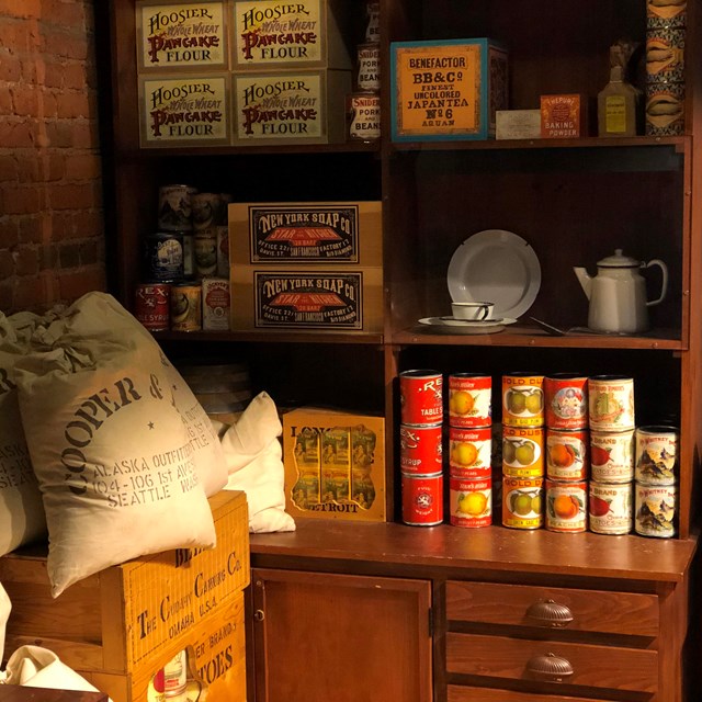 Sacks of supplies sit next to cans on wooden shelves
