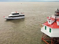 Tour boat near the Thomas Point Shoal Lighthouse with a red roof. Cloudy sky and calm water.