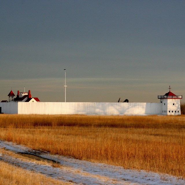 Trading post in grassland surrounded by tall white fence