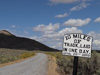 Gravel road through green, yellow and brown sagebrush landscapes, Historical sign on side of road
