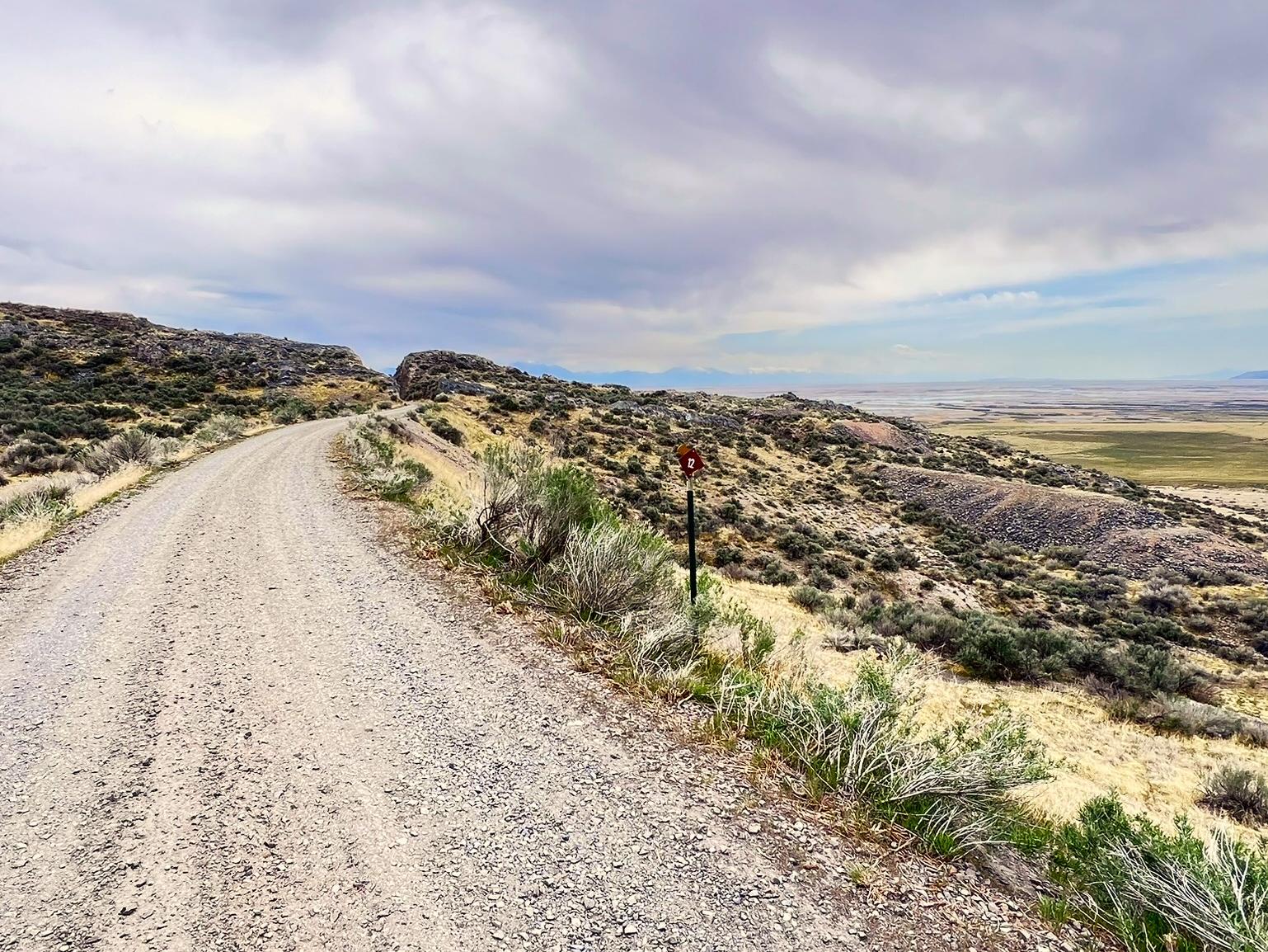 Gravel road among yellow and green sagebrush, views of vast valley mountains in distance