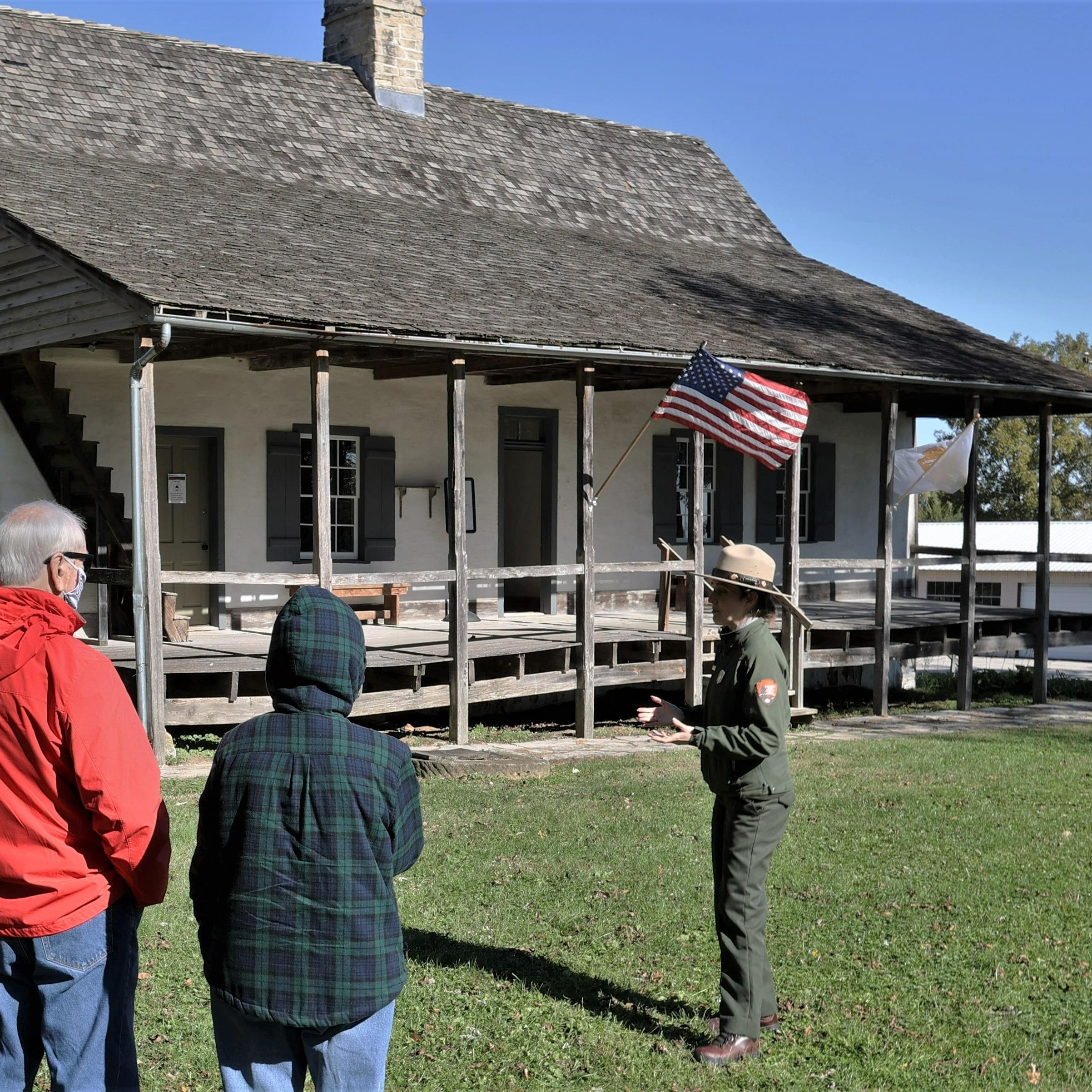 Park Ranger giving a tour in front of a old home with a front porch. 