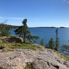 View of rocky outcropping surrounded by trees along water with islands in the distance. 