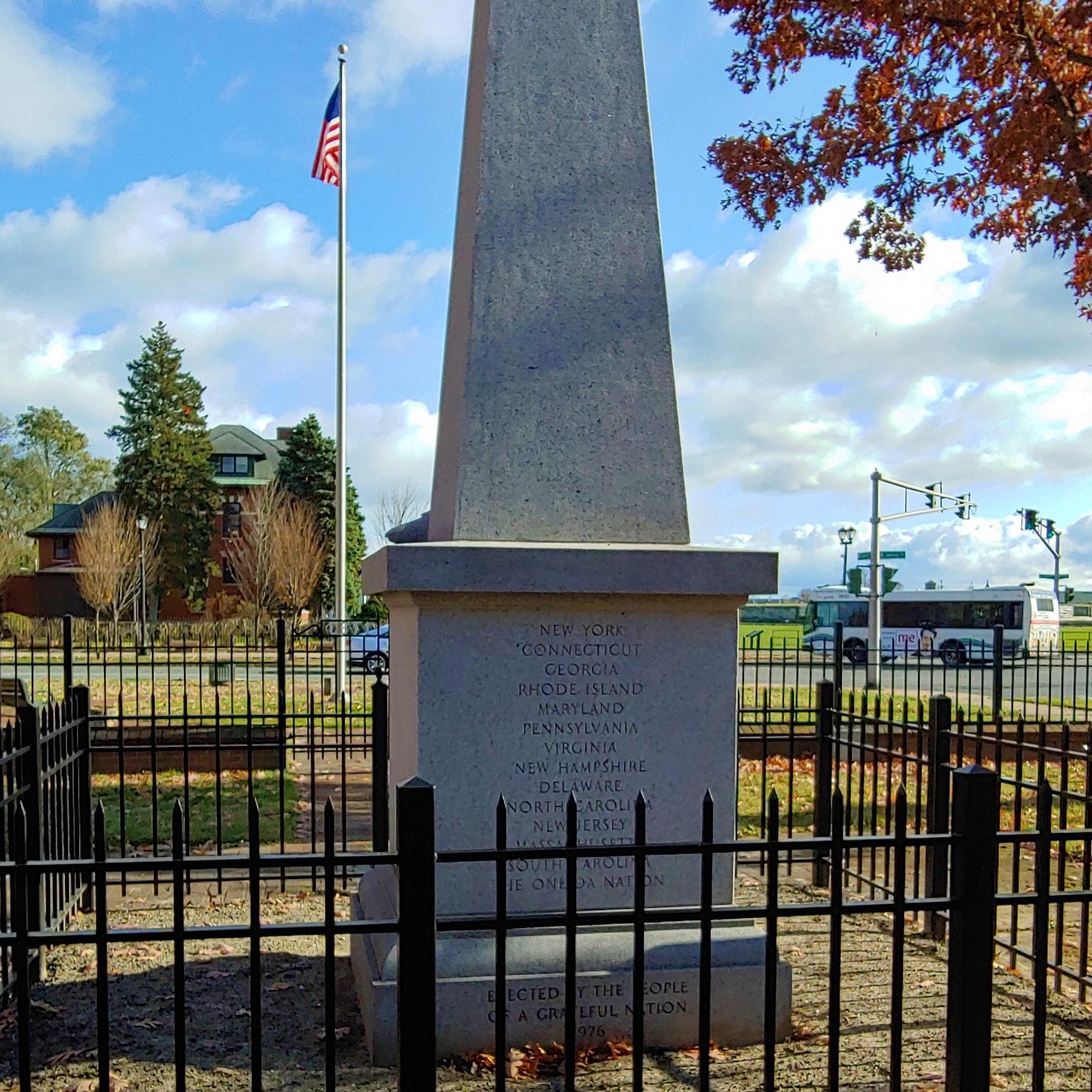A view of a 20 foot tall, granite obelisk. It has words etched into the back. 