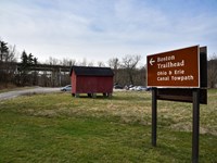 Road sign points to unpaved parking lot with a red corn crib, center, and distant highway bridges.