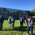 A group of students stand around a ranger talking in front of a mural depicting pullman themes.