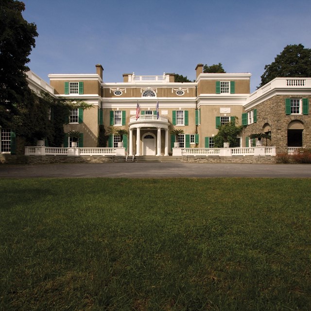 A three-story house on a lawn surrounded by trees.