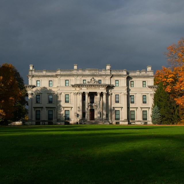 A large limestone mansion on a vast green lawn surrounded by orange trees.