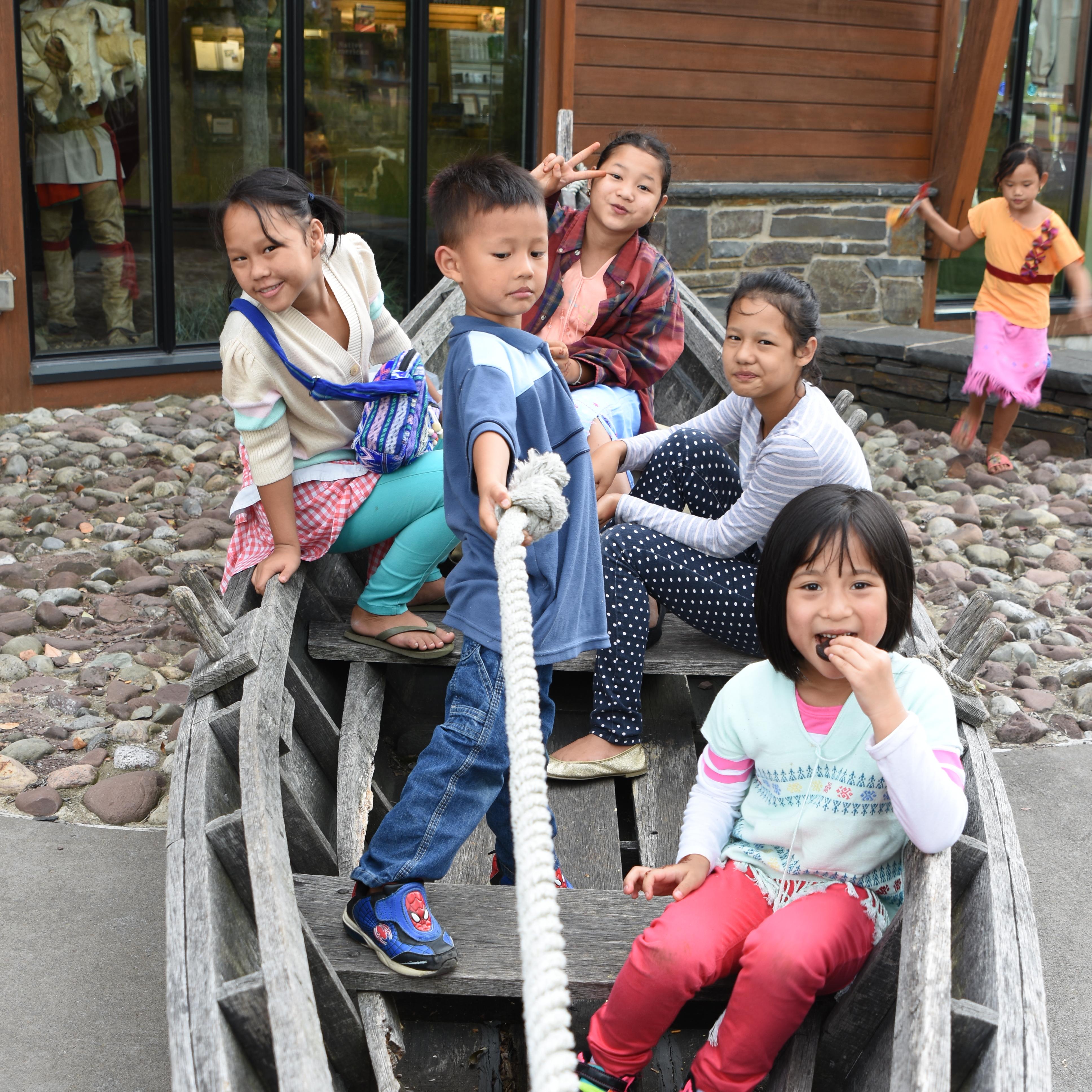 Several kids sit crowded together in a bateau-style boat. 