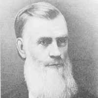 A black and white portrait of a white man in a suit with a long white beard and hair combed back