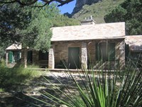 A cabin with stone walls and roof surrounded by desert mountain landscape and plants