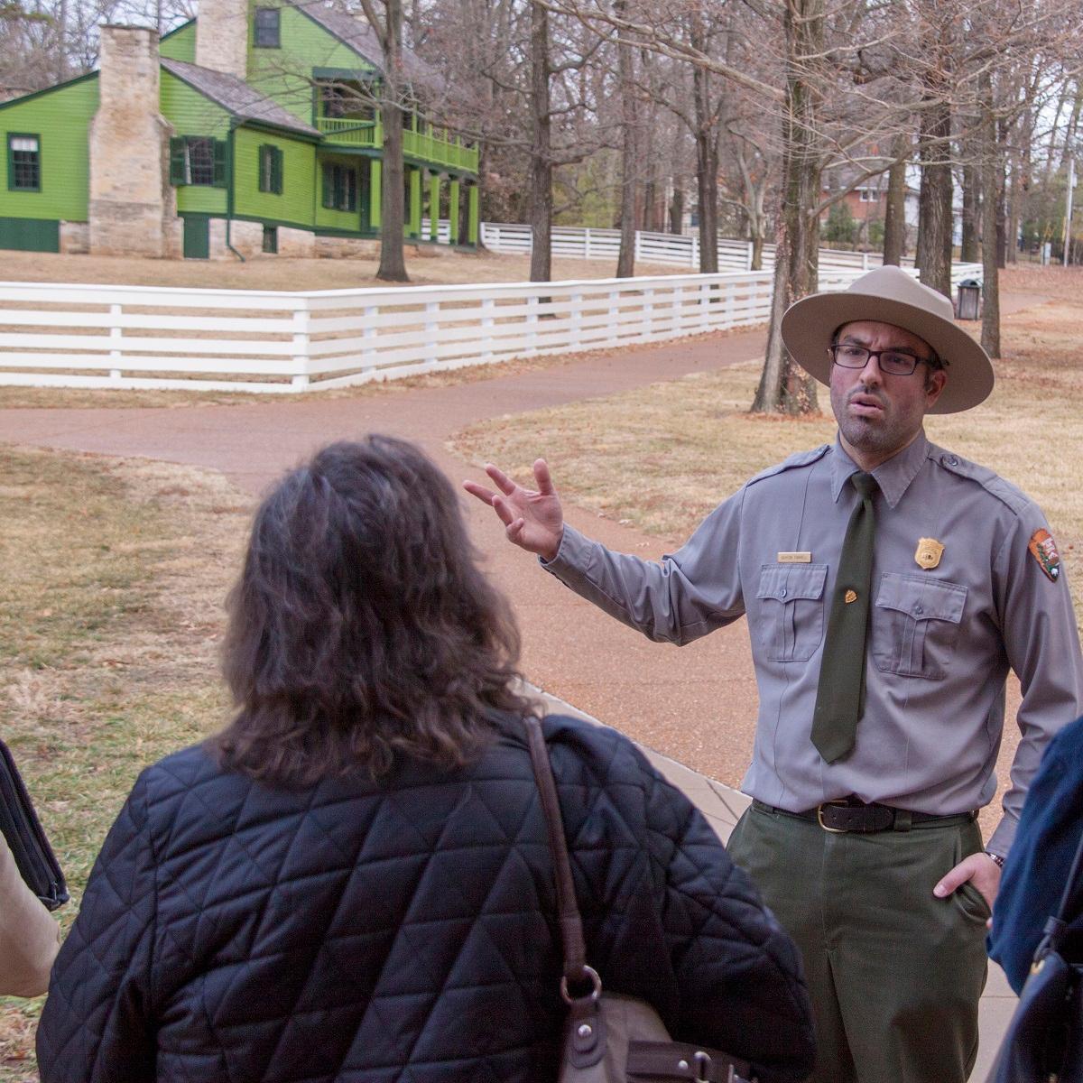Park Ranger standing in front of a group of people with a green house in the background.
