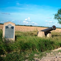 Stone historical marker and replica cannon by the roadside.