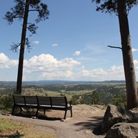 A bench along a trail overlooking a valley.