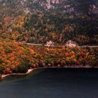 A road goes through brightly colored leaves around a mountain above a lake.