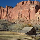 A barn in a grassy field surrounded by towering red cliffs.
