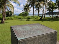 Bronze plaque set on a concrete cube. In the background are palm trees and the ocean.
