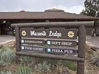 Wooden sign in front of single story lodge building reads Maswik Lodge, Registration, Gift Shop etc.
