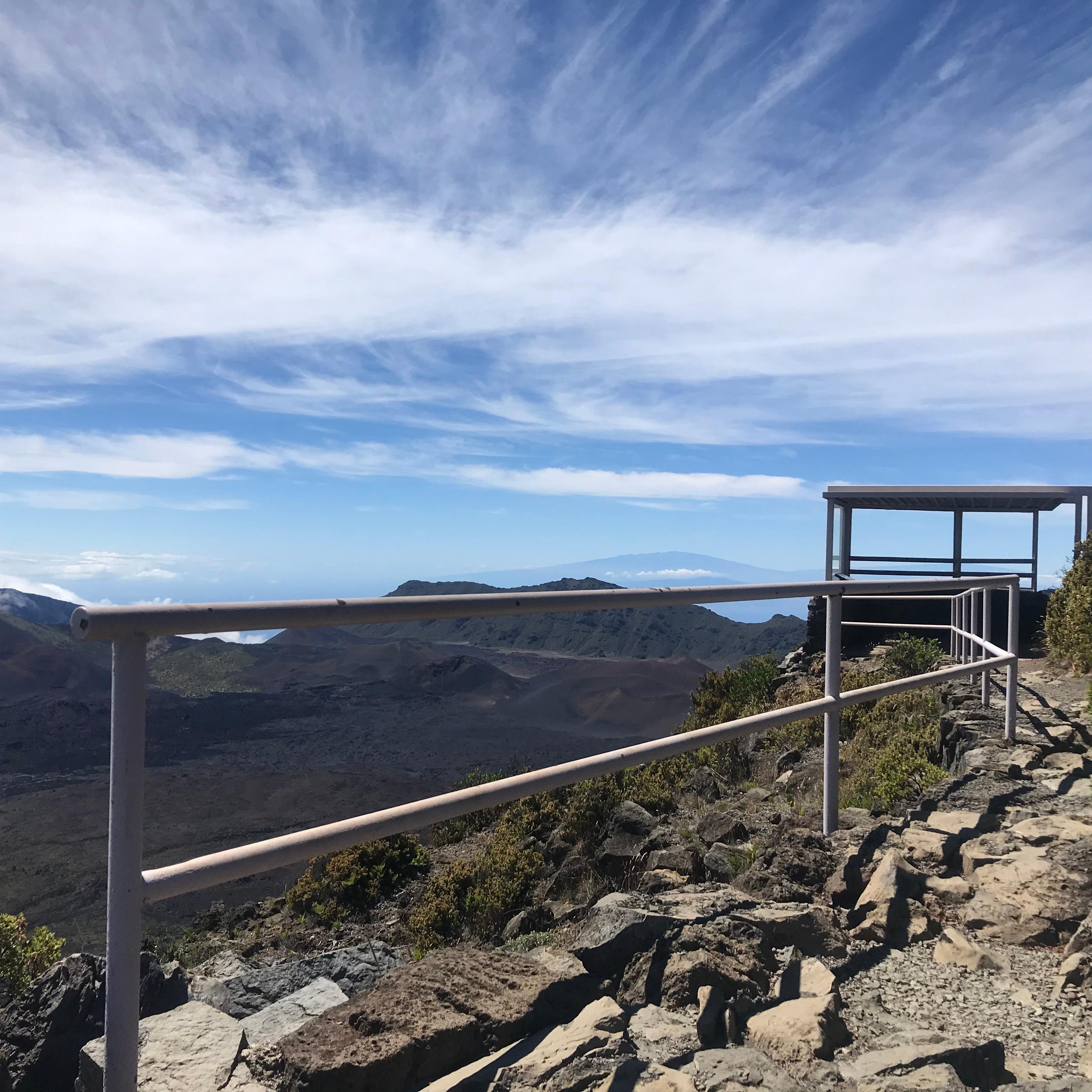 A path with a railing leads to an overlook next to a deep volcanic valley
