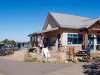 Rows of bicycles in front of a small single story building with a peaked roof and shade awnings.