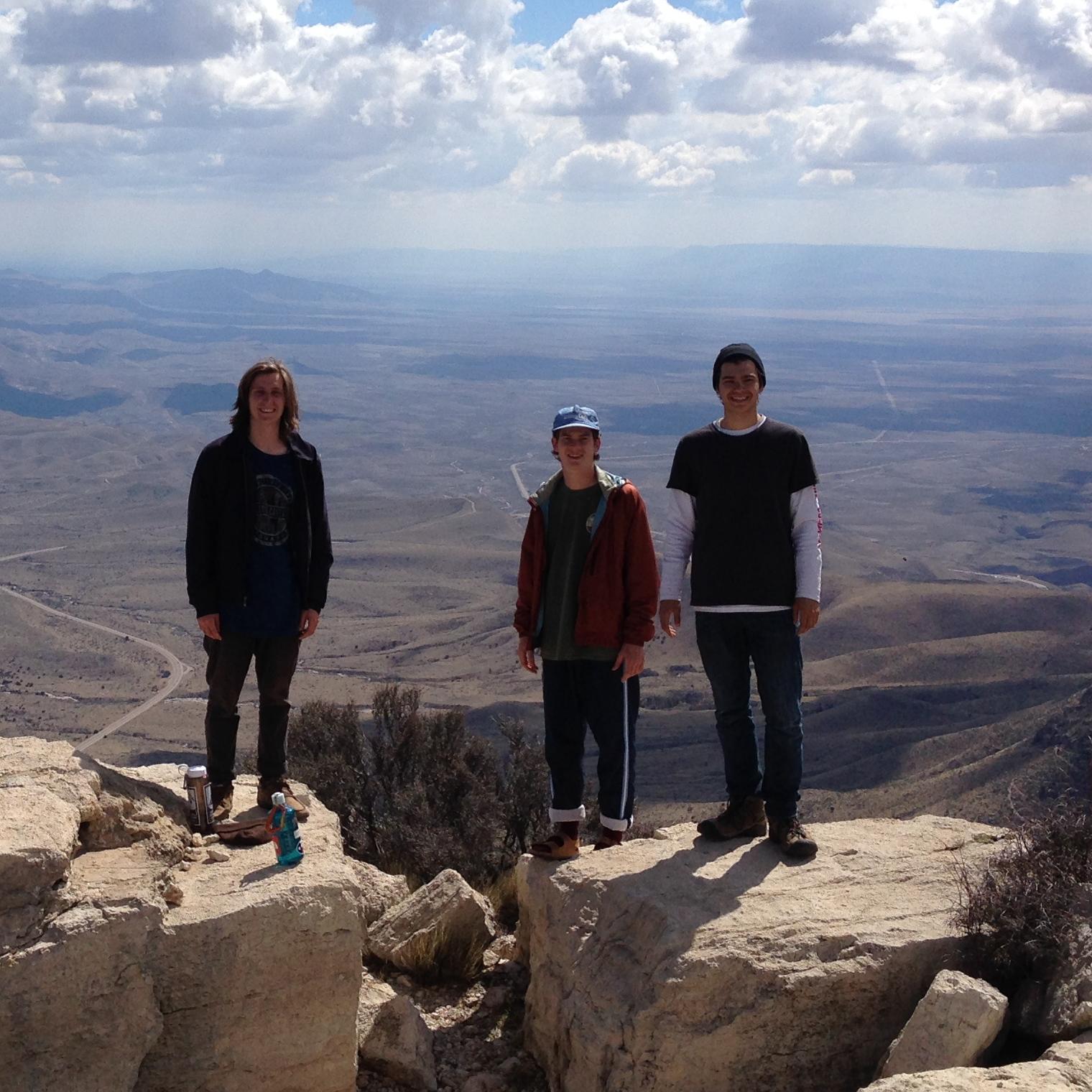 Three people stand on the summit of a mountain peak