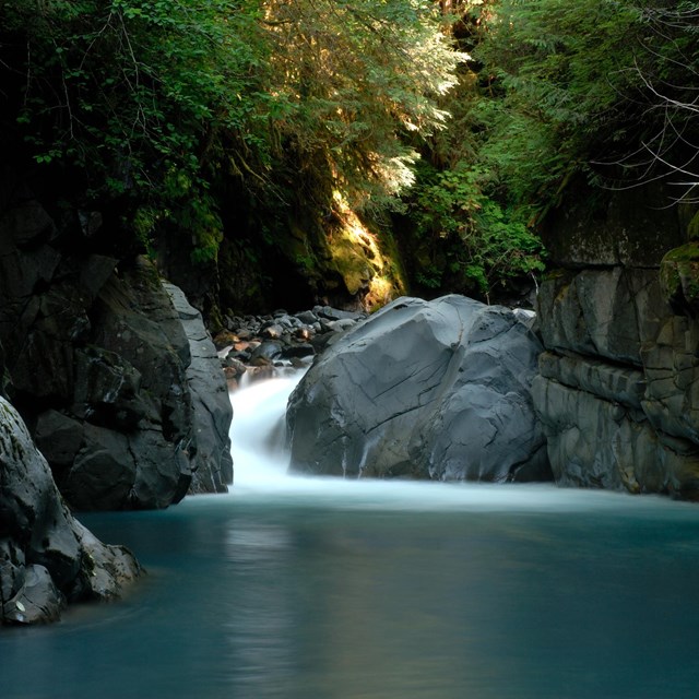 A waterfall above a calm body of water between craggy rocks.