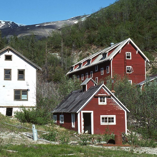 Three abandoned buildings, one white and two red, on an Alaskan hillside