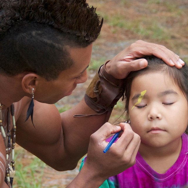 American Indian man paints the face of an American Indian girl. 
