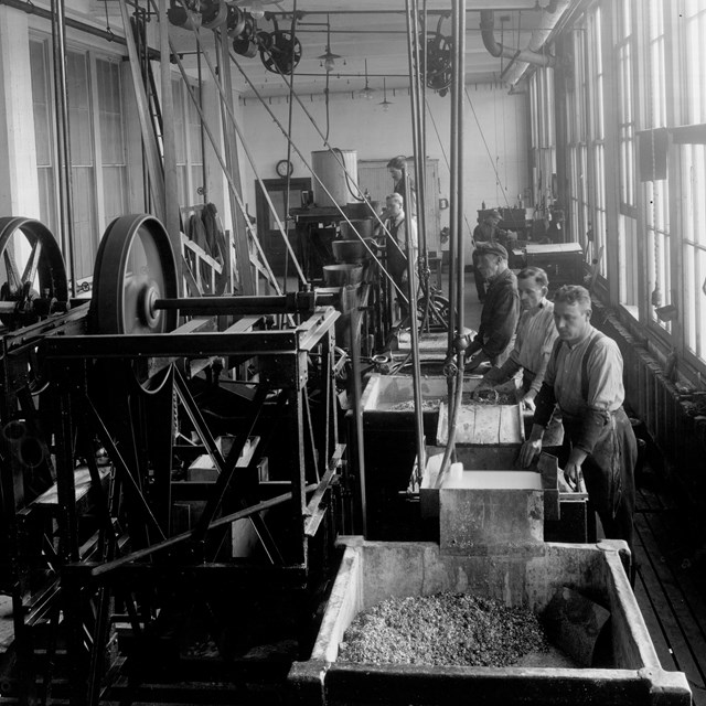Black and white image of men lined up at machines in a factory