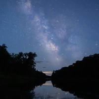 The Milky Way and many stars illuminate the night sky over the river.