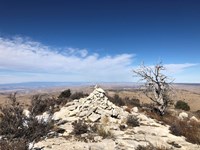 A stone cairn marks a summit with a vast desert landscape beyond