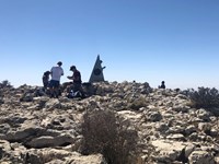groups of people sit and stand on a stony summit.