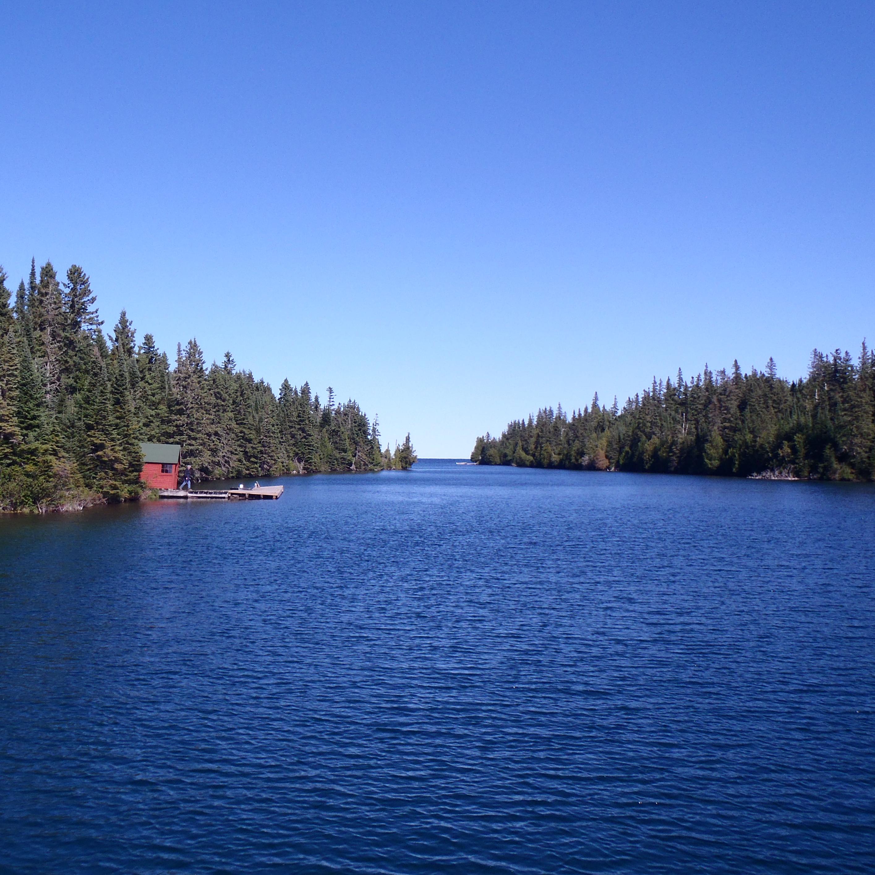 A red historic summer cottage mail room and dock can be seen along the conifer lined Tobin Harbor. 