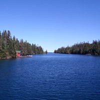 A red historic summer cottage mail room and dock can be seen along the conifer lined Tobin Harbor.