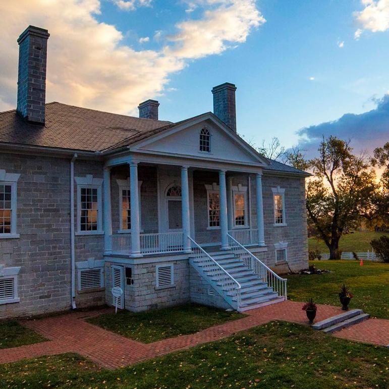 The rising sun lights the clouds over an antebellum stone mansion with a white portico.