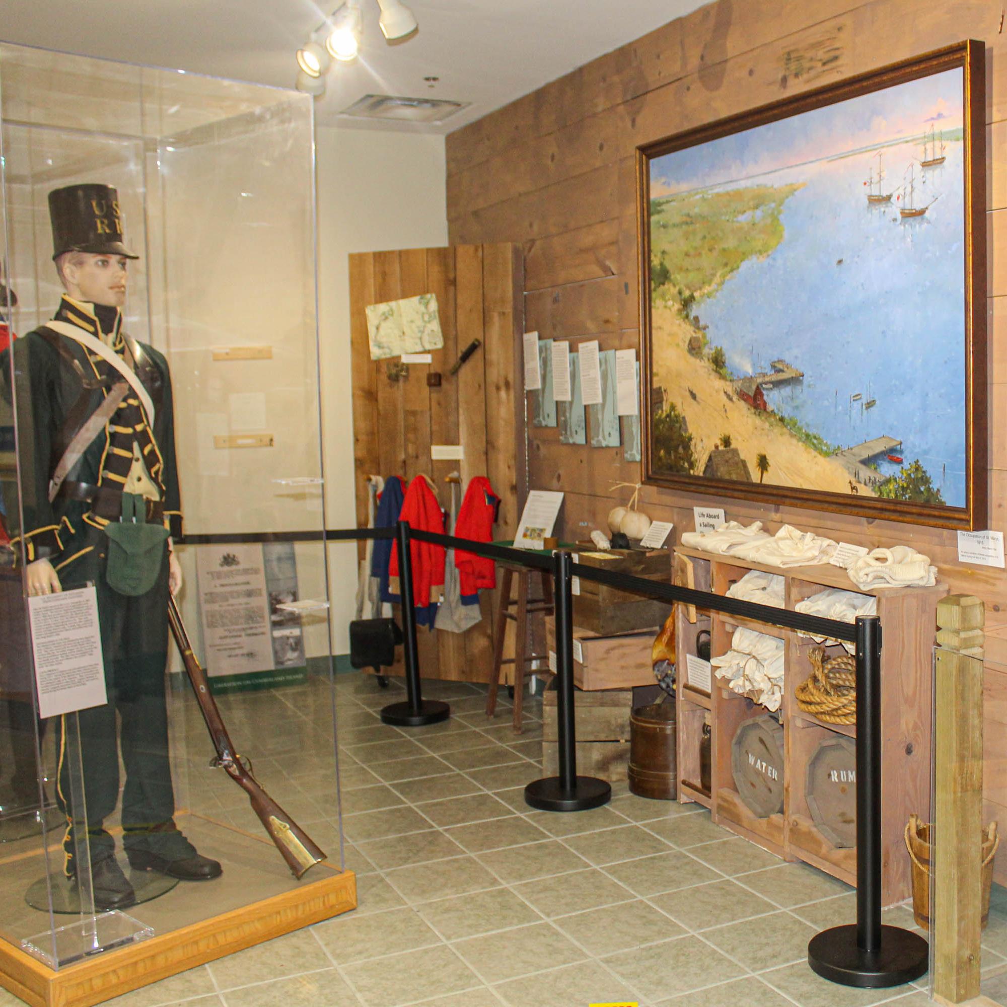 A museum display with manikins in uniforms, a historic painting and a large anchor on the wall. 