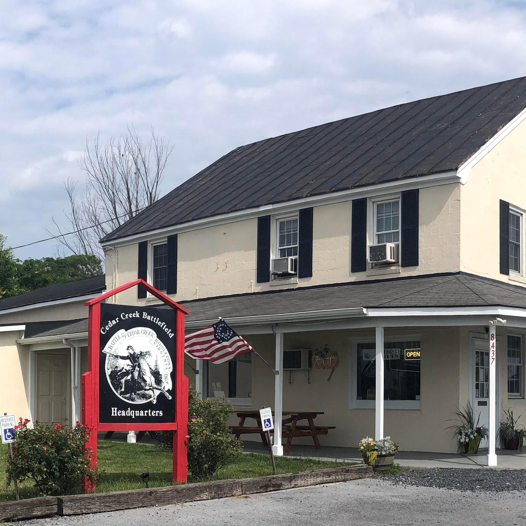 A white farmhouse-like building stands on a rural property with a large sign in front. 
