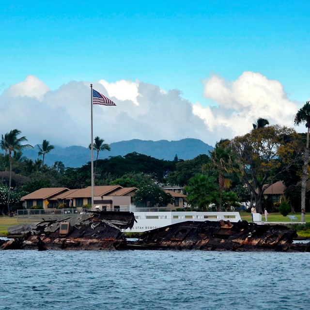 shipwreck rusts in ocean in the foreground with tropical mountains and palm trees beyond