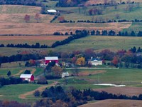 Barns and old plantation buildings among farms on a valley floor are seen from a mountain overlook.