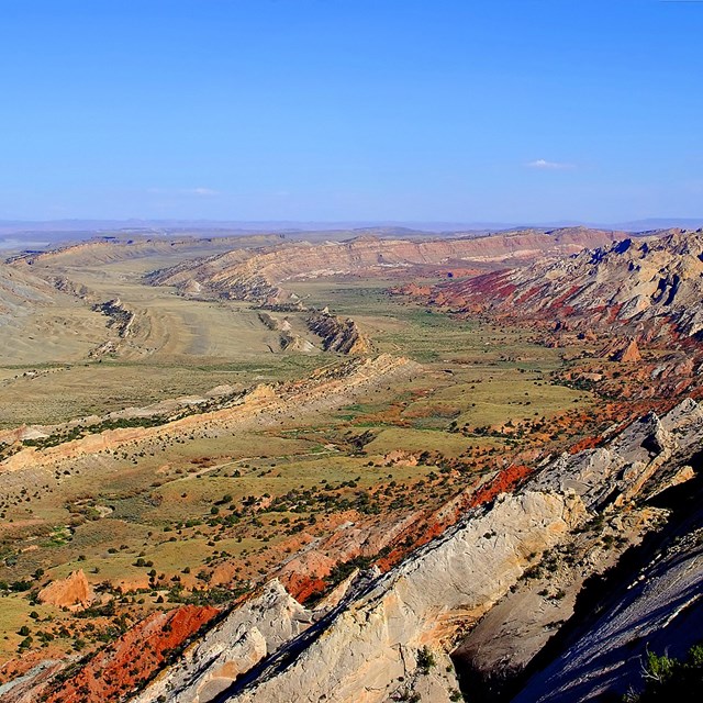 many different layers of rock angled up with a green valley in the center