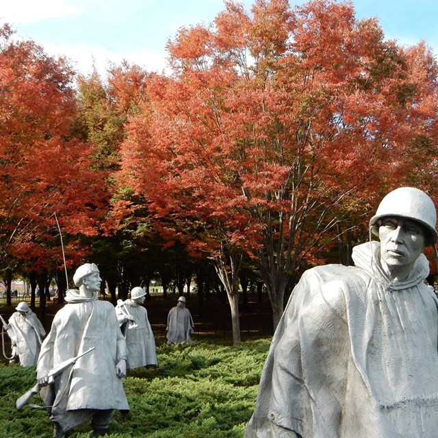 Statues of soldiers in garden with red trees in background
