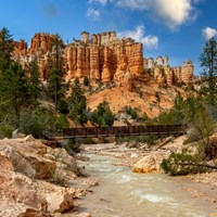 A creek meanders through red rocks with red rock formations in the background.