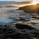 Waves crash on rocky ocean coastline at sunset