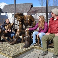 Three visitors sat next to a bronze statue of a gold prospector and his dog