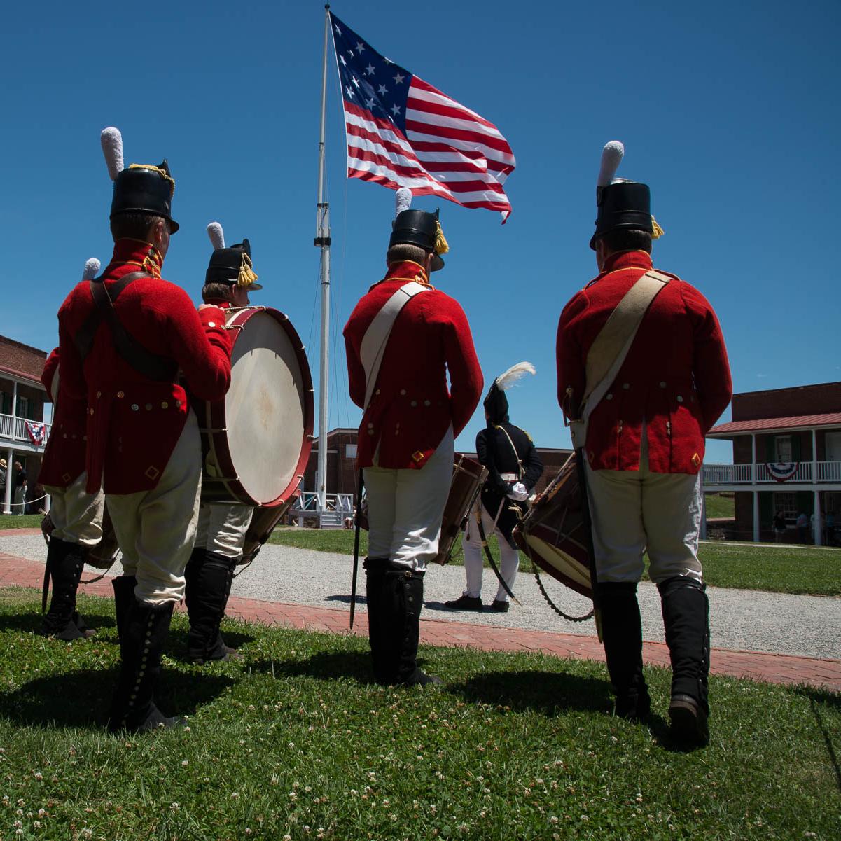 A group of living historians stand in the fort with the large garrison flag flying in the background