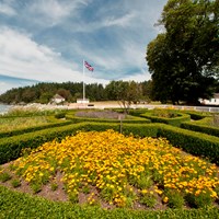 A formal garden with flowers and manicured hedges in front of historic English military buildings.