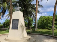 A beige obelisk with a metal plaque attached to the front and the bust of a man on the top.