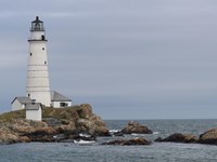 A tall white lighthouse with smaller white buildings at its foot along a rocky coastline.