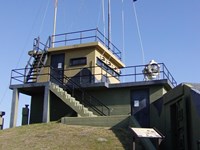 Concrete structure with signal flags flying. Grassy hill in foreground with a sign.