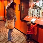 A child and parent looking at a blacksmith\'s hammer in an exhibit case
